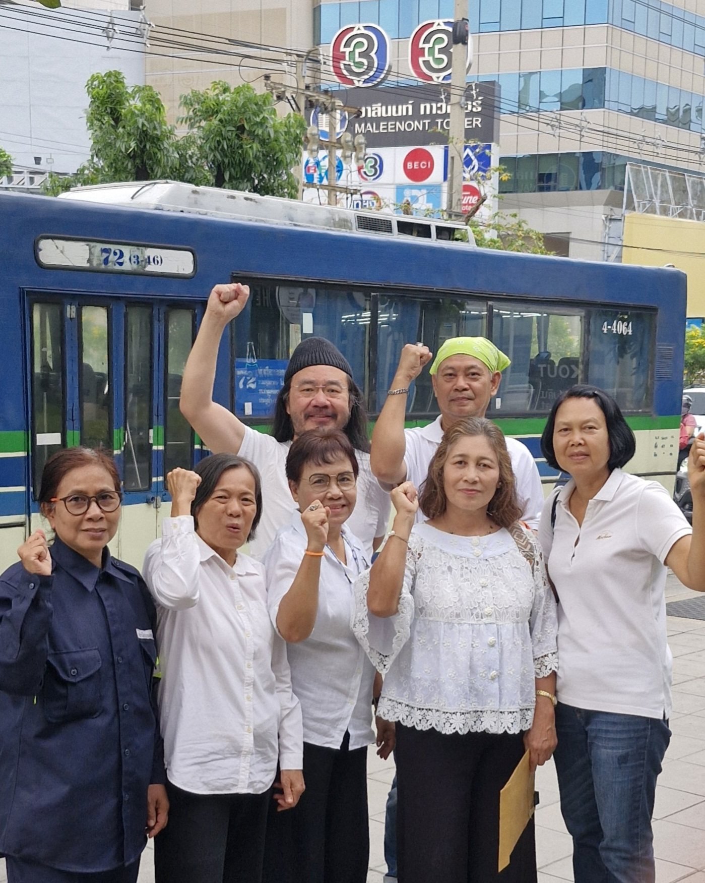 33 Thai workers in white shirts raise their fists in front of Channel 3's Maleenont Tower, Bangkok